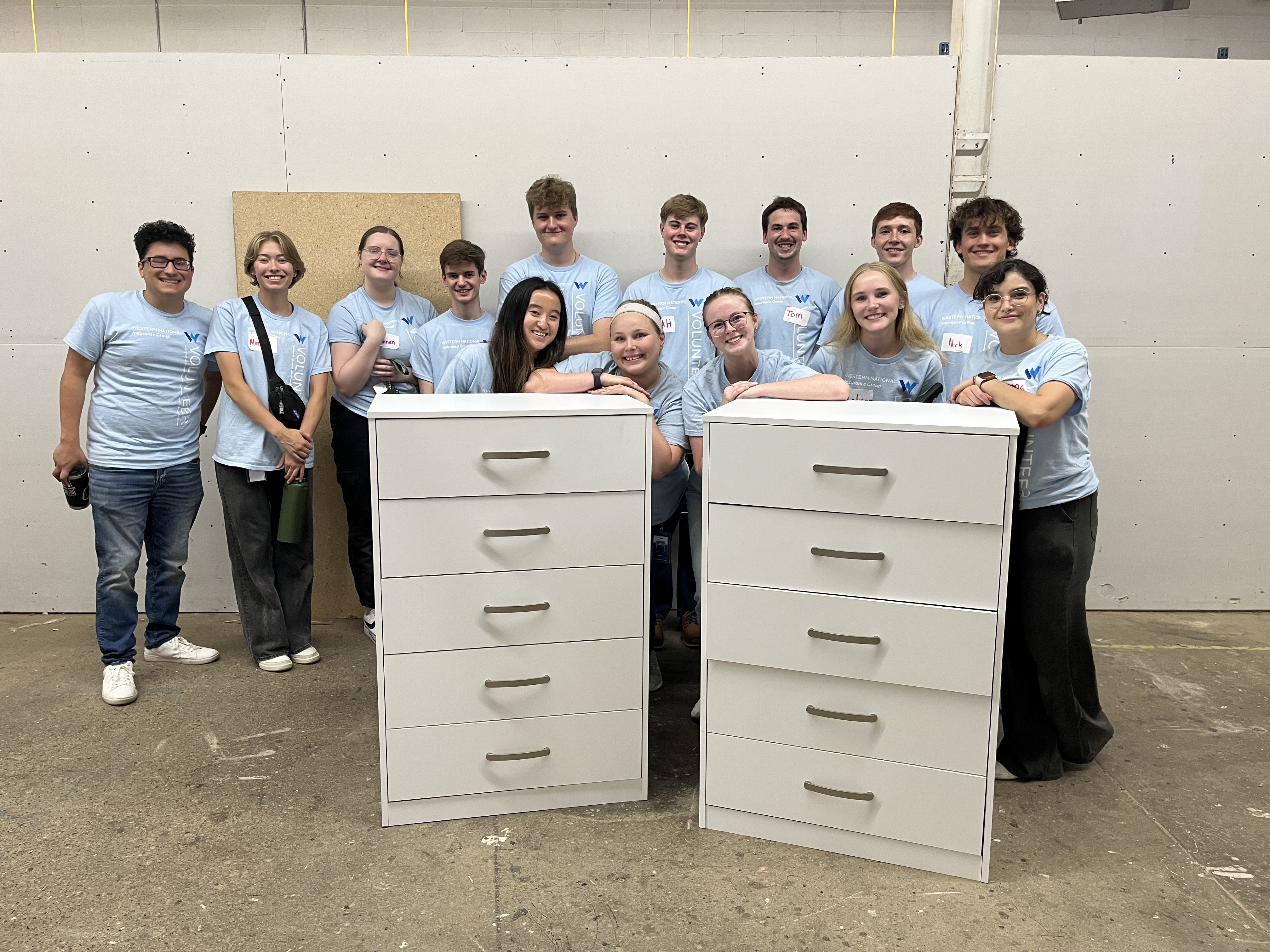 Western National's 2024 summer interns standing behind the dressers they built at the Bridging Dresser Build volunteer event.