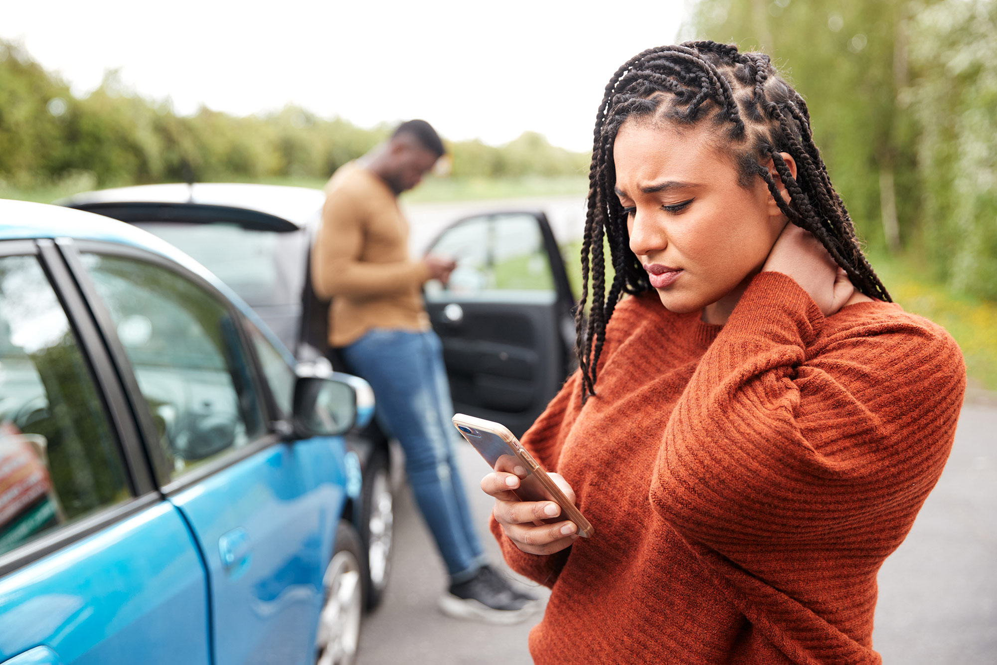 Two drivers looking at their respective phones after being involved in a car accident with each other.