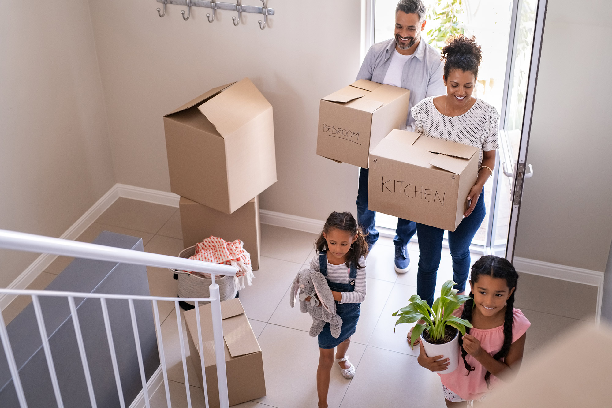 Family carrying moving boxes and items through the front door.