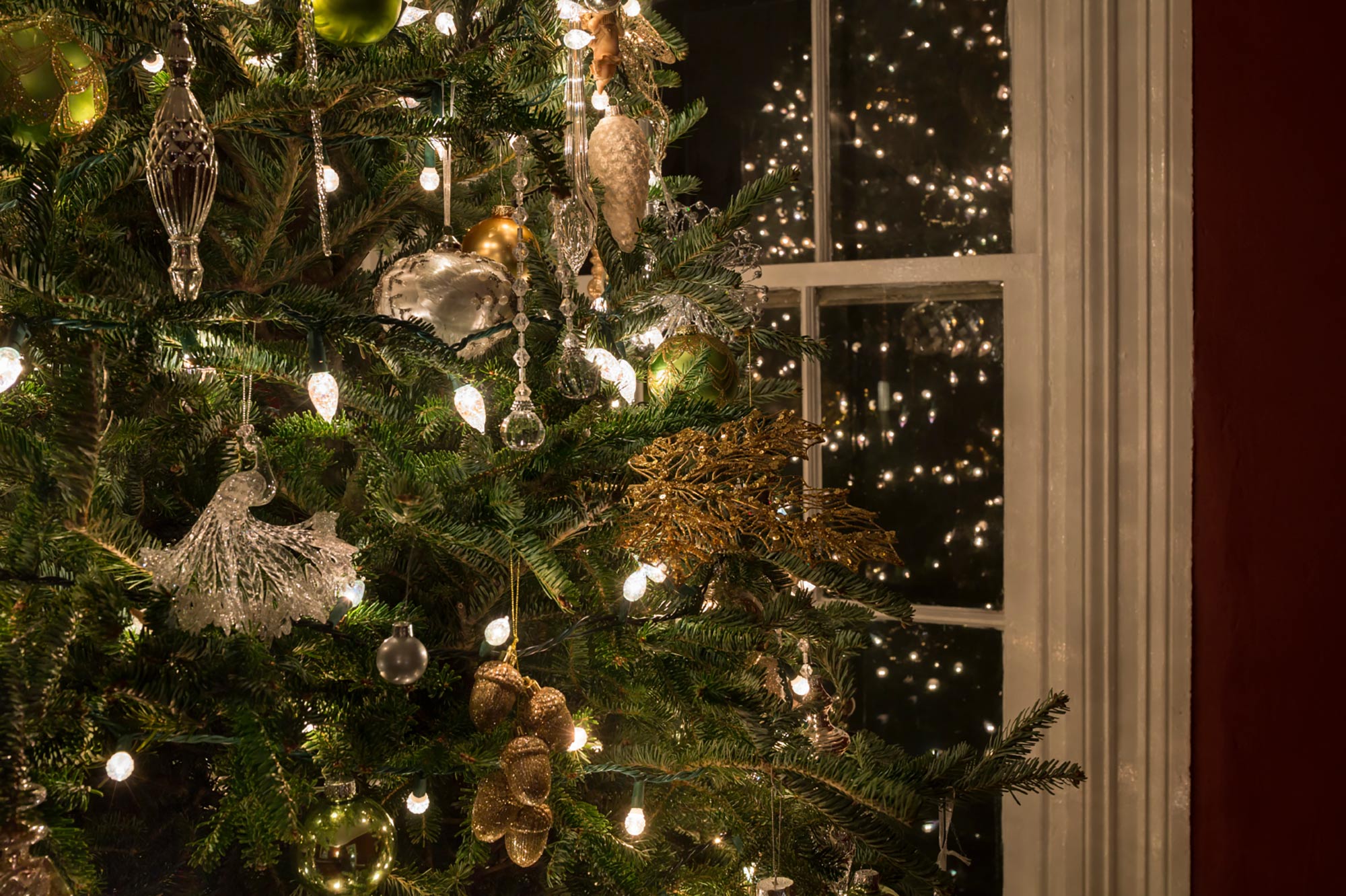 Christmas tree with silver and gold decorations and white illuminated lights in front in a home.