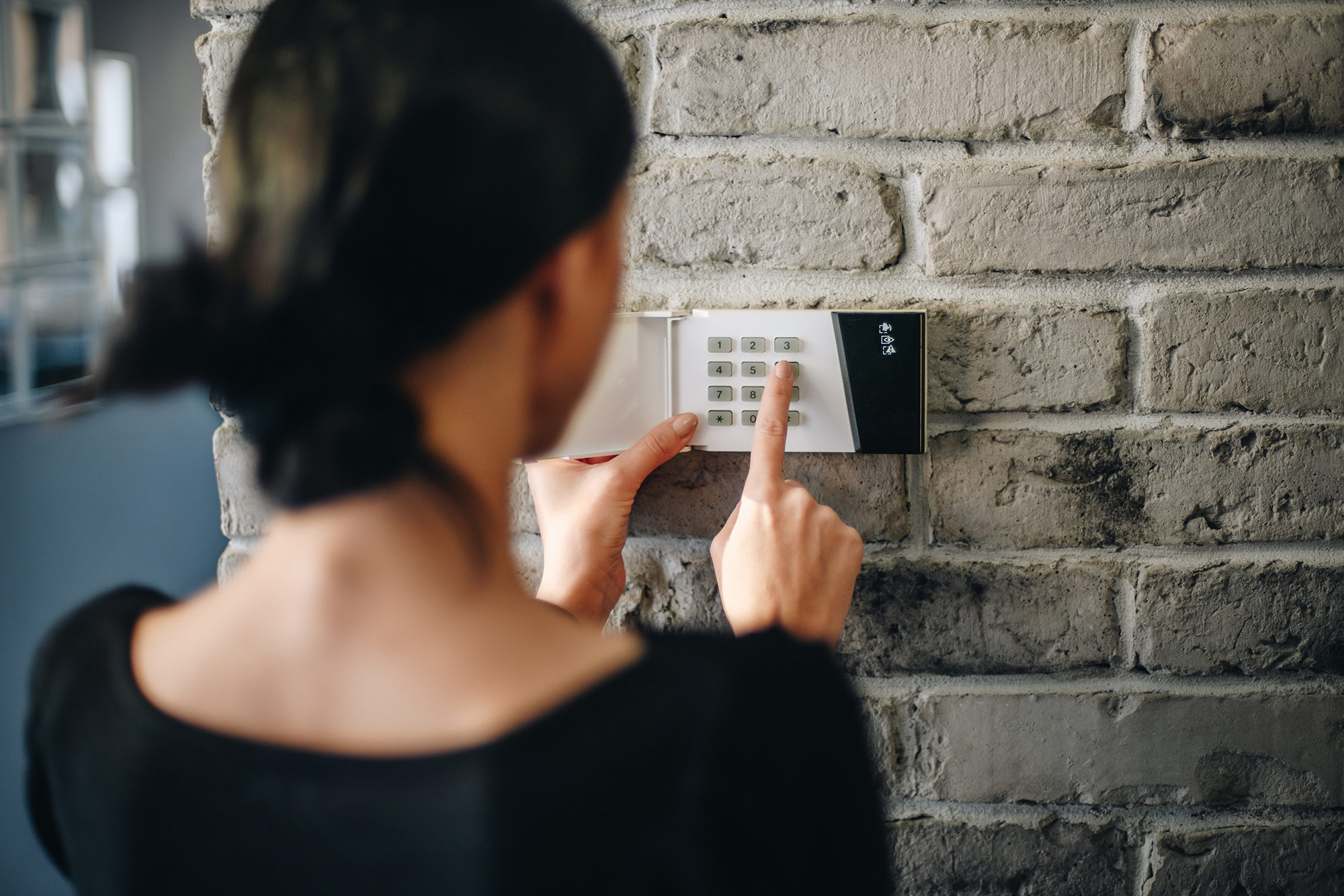 Over-the-shoulder view of woman entering code into wall-mounted home security system panel