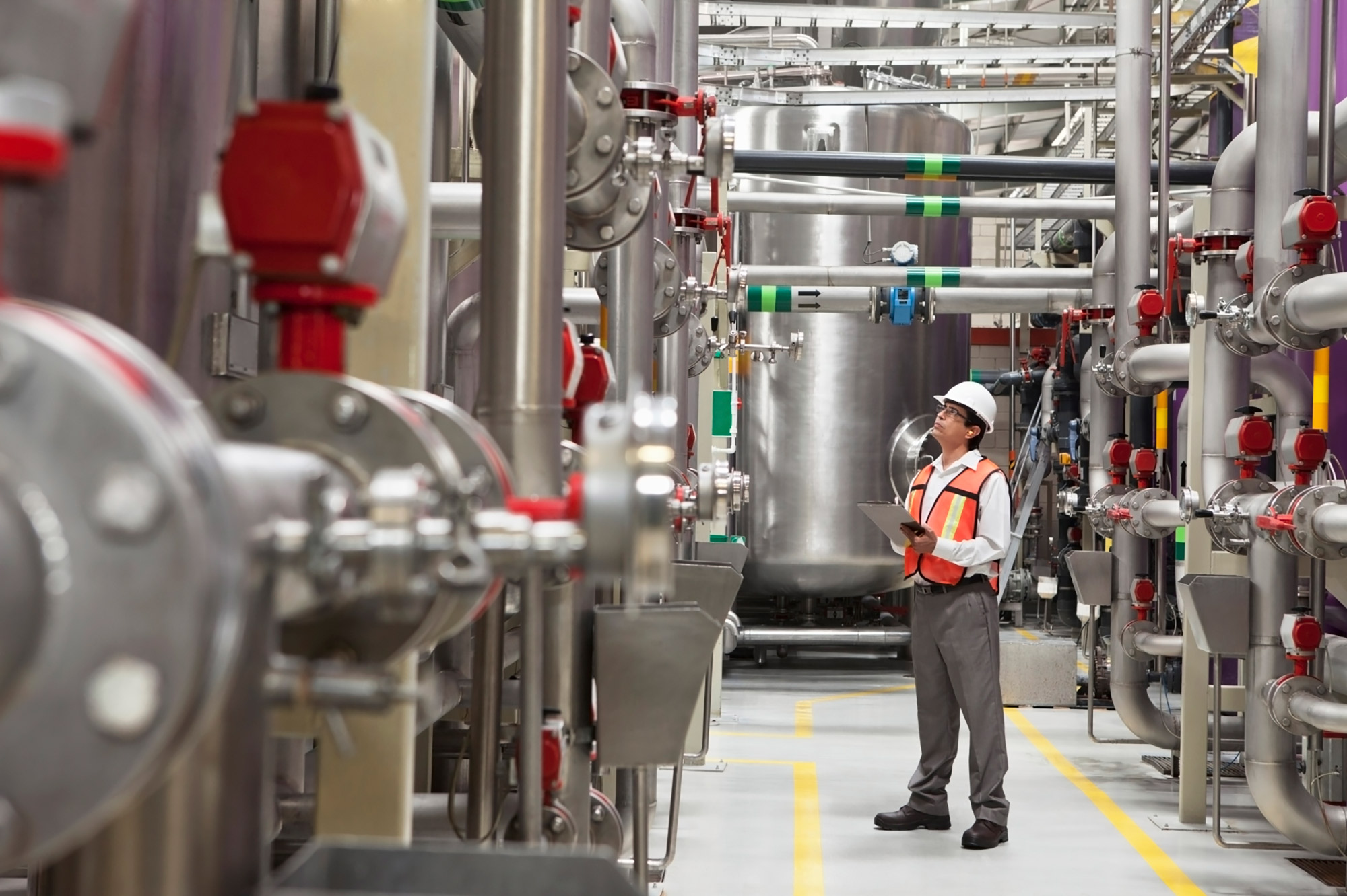 Man in hard hat and safety vest standing in industrial setting.
