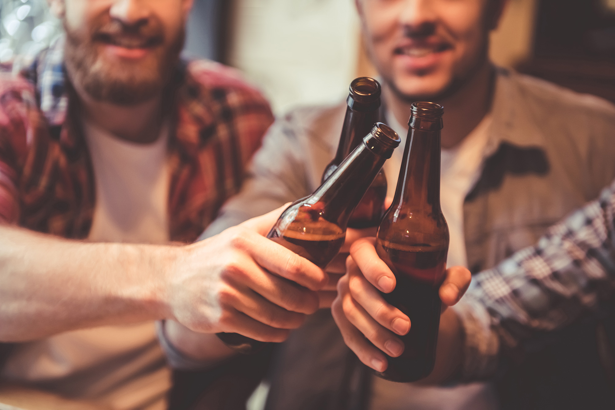 Close-up of three people clinking their beer bottles together.