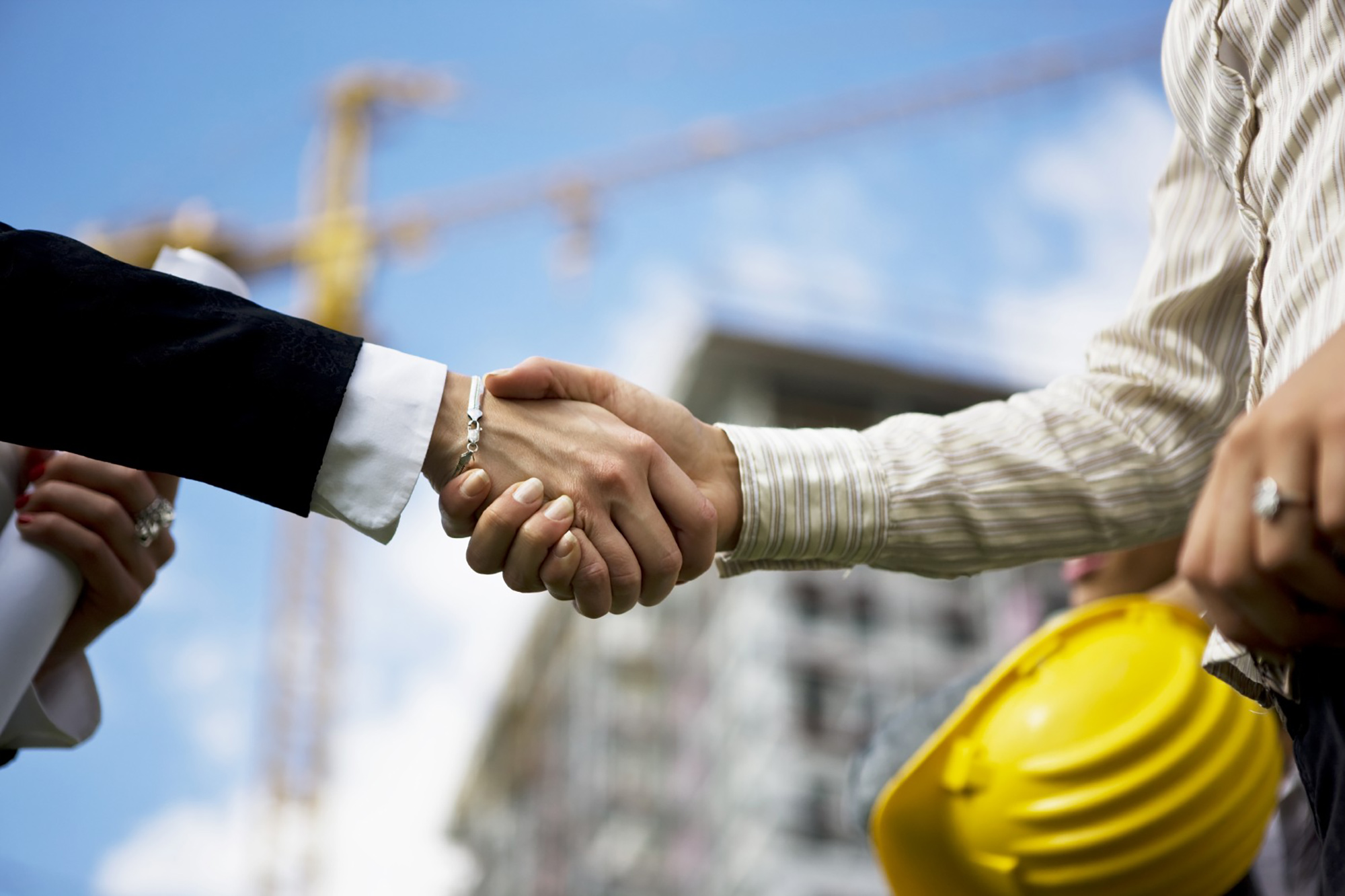 Two people shaking hands in front of a construction site.