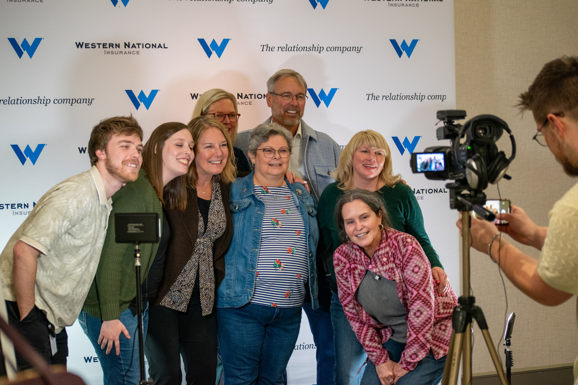 A group of employees crowded to gether in front of a photographer to get their photo taken.