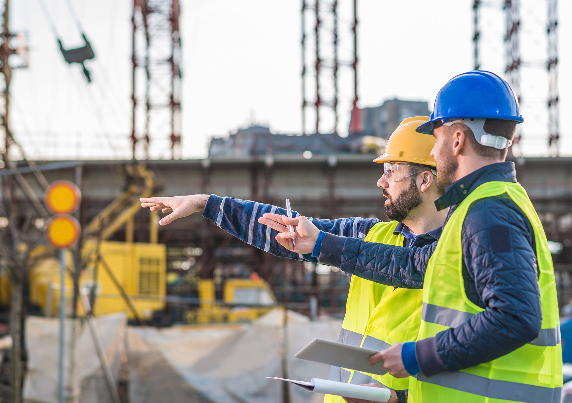 Two men in appropriate PPE overlooking a construction site.