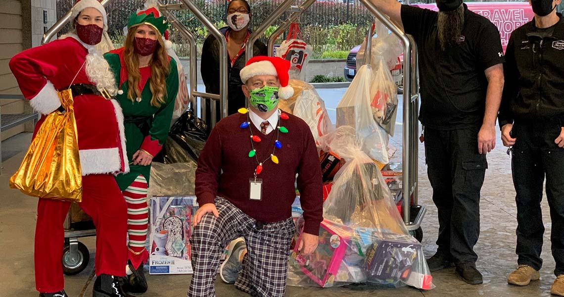 Group of Western National employees wearing face masks and dressed up in holiday accessories and costumes, including an elf and Santa, displaying bags of children's toys to be donated.