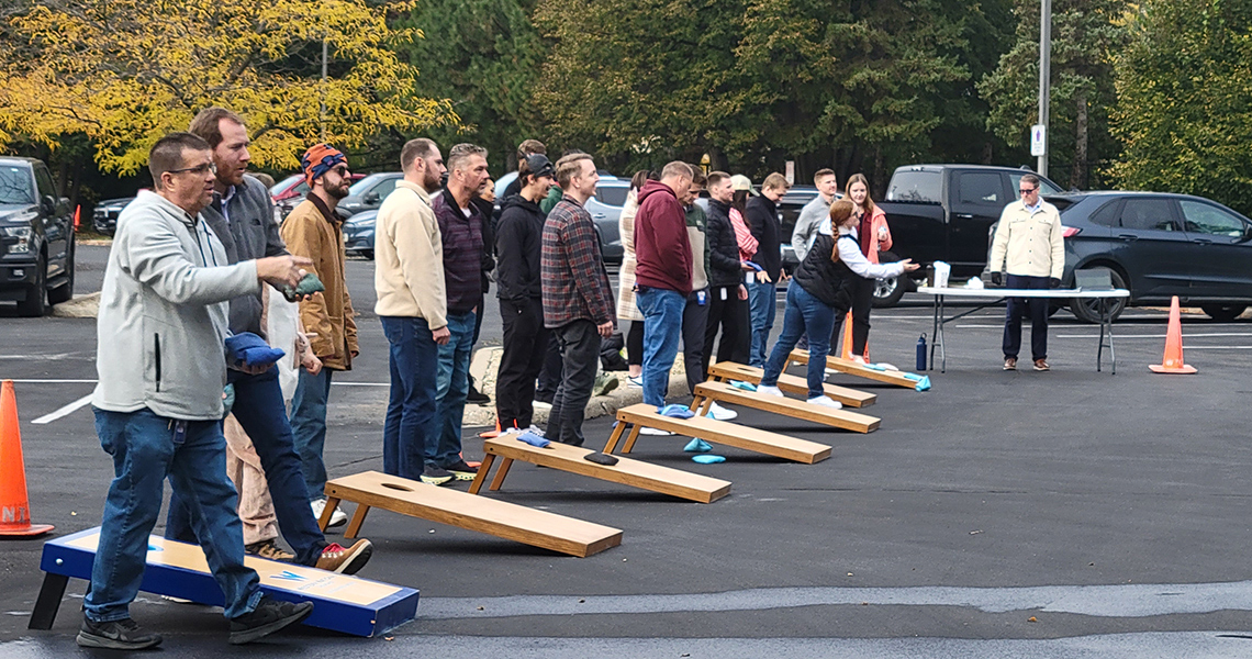 Candid shot of a Western National employee outdoors tossing an orange, plastic ping pong ball towards a row of plastic cups as other employees look on.