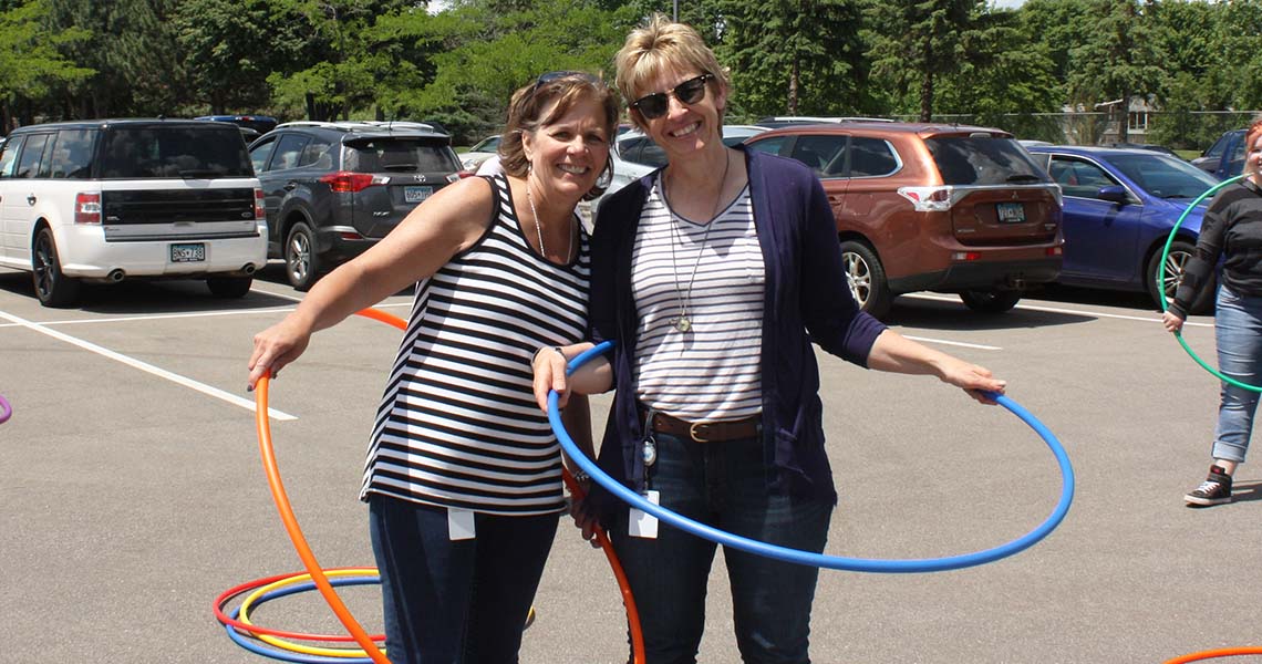 Two Western National employees with hula hoops posing together for a photos while outdoors on a sunny day.