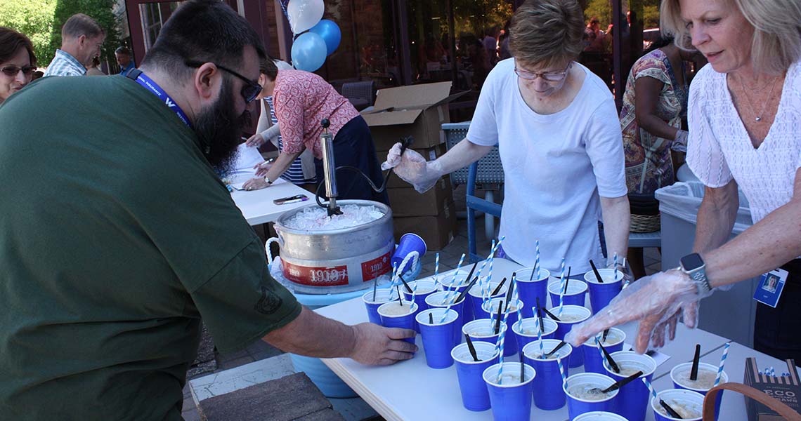 Candid shot of Western National employees being served rootbeer floats outdoors.