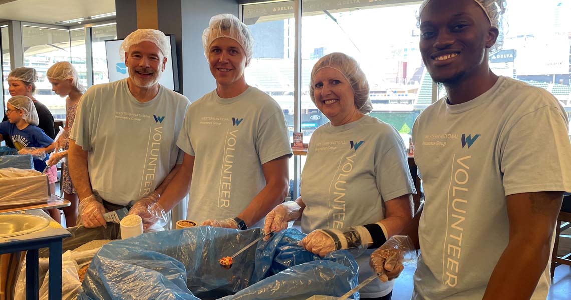 Group photo of four Western National employees wearing matching Western National branded t-shirts serving food at a volunteer event. 