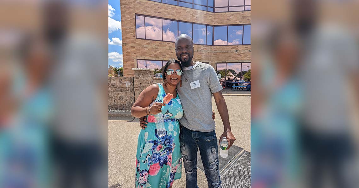 Two smiling Western National employees posing together outdoors on a sunny day with the exterior of Western National's Edina office building in the background.