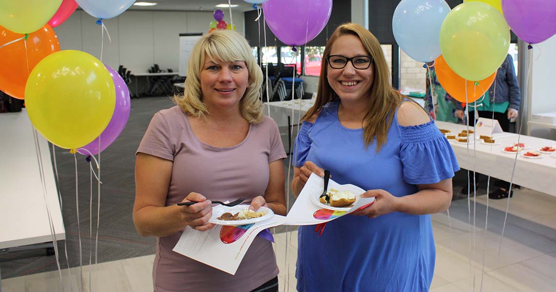 Two Western National employees standing in the foyer of Western National's Edina office holding slices of pie on plates with balloons in the background.