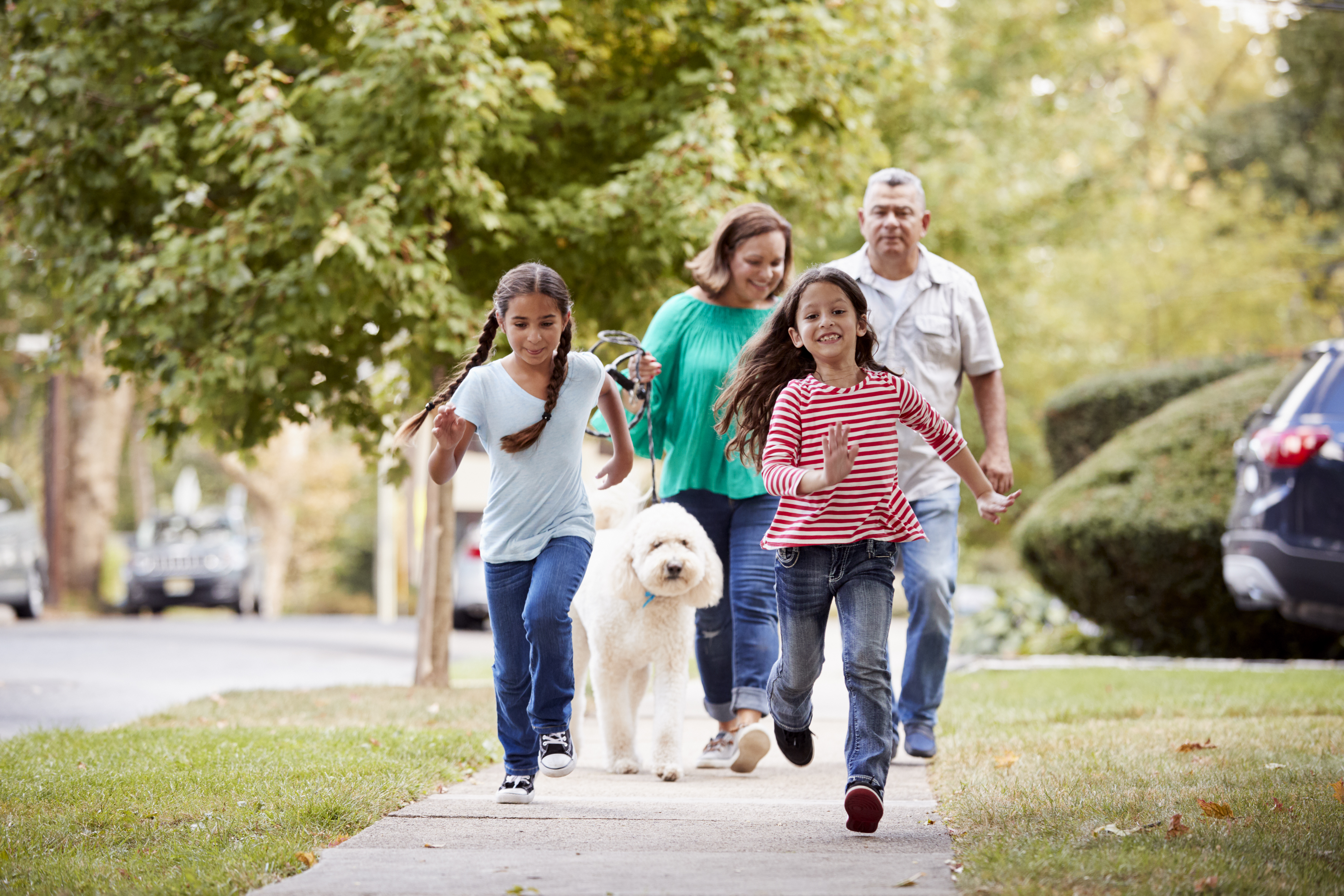 Family walking their dog together on a residential neighborhood sidewalk.