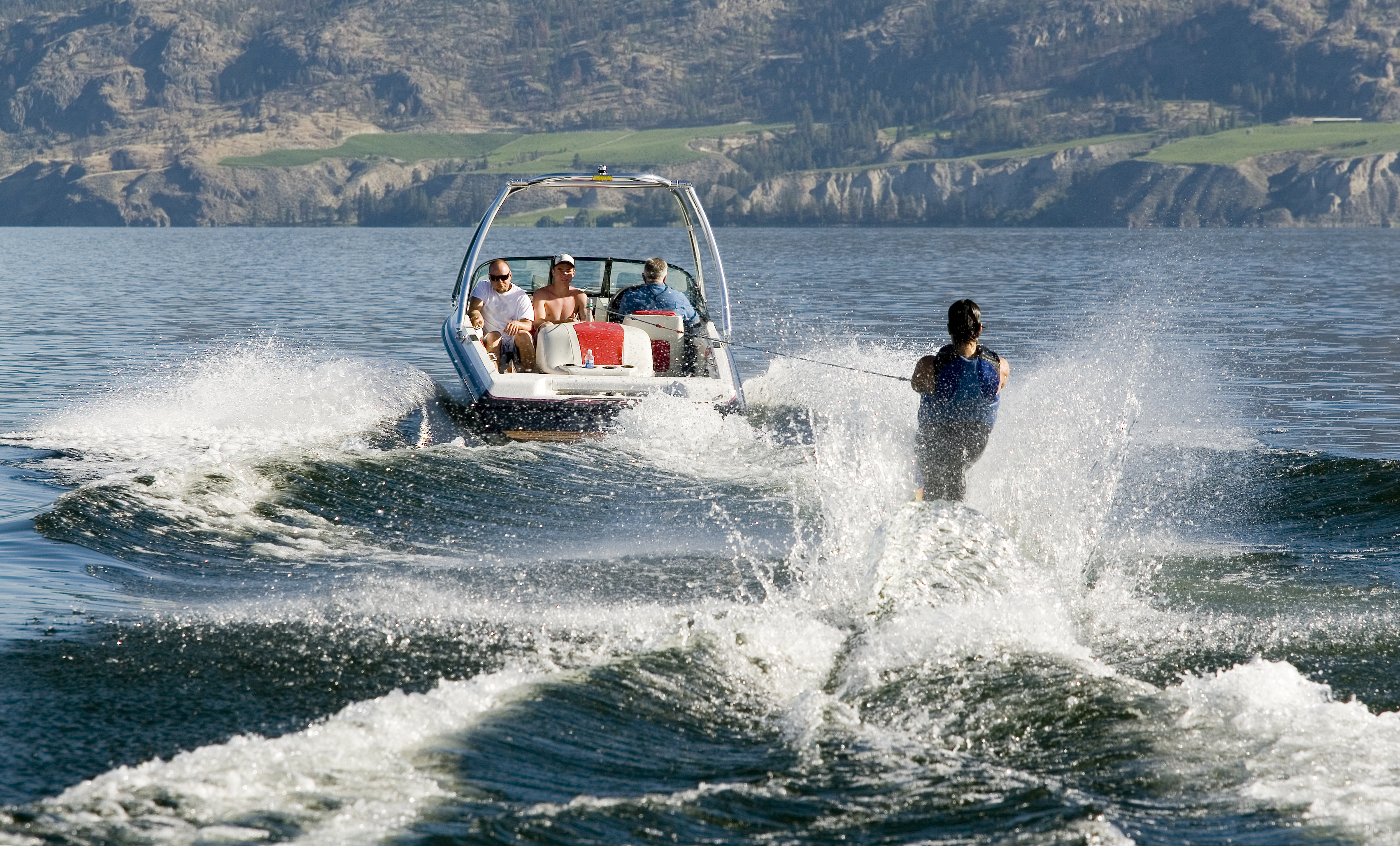 Speedboat pulling a water skier across a lake with mountains in the background.