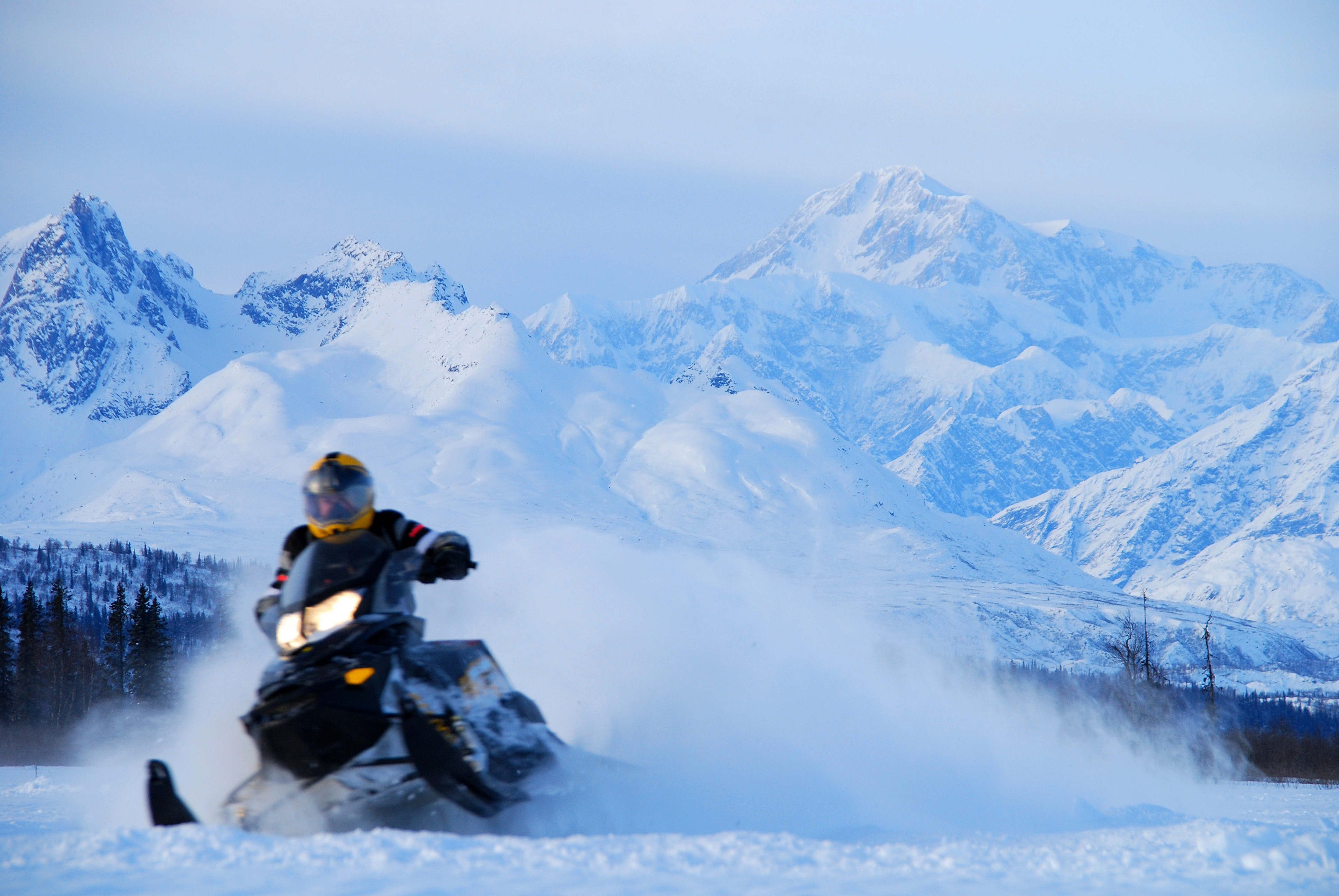 Person on snowmachine with Alaskan mountains in the background.